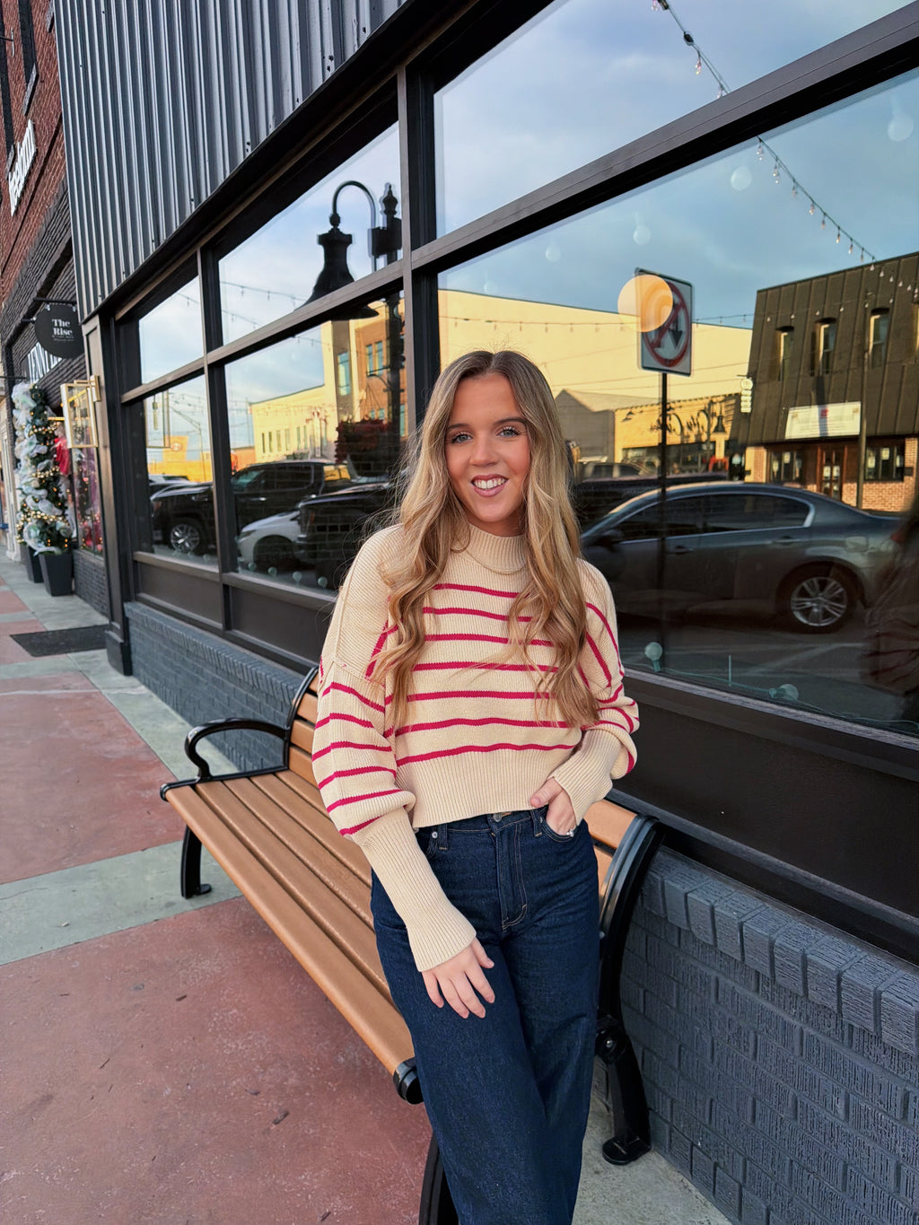 Woman in a striped sweater and jeans standing on a sidewalk with a building in the background