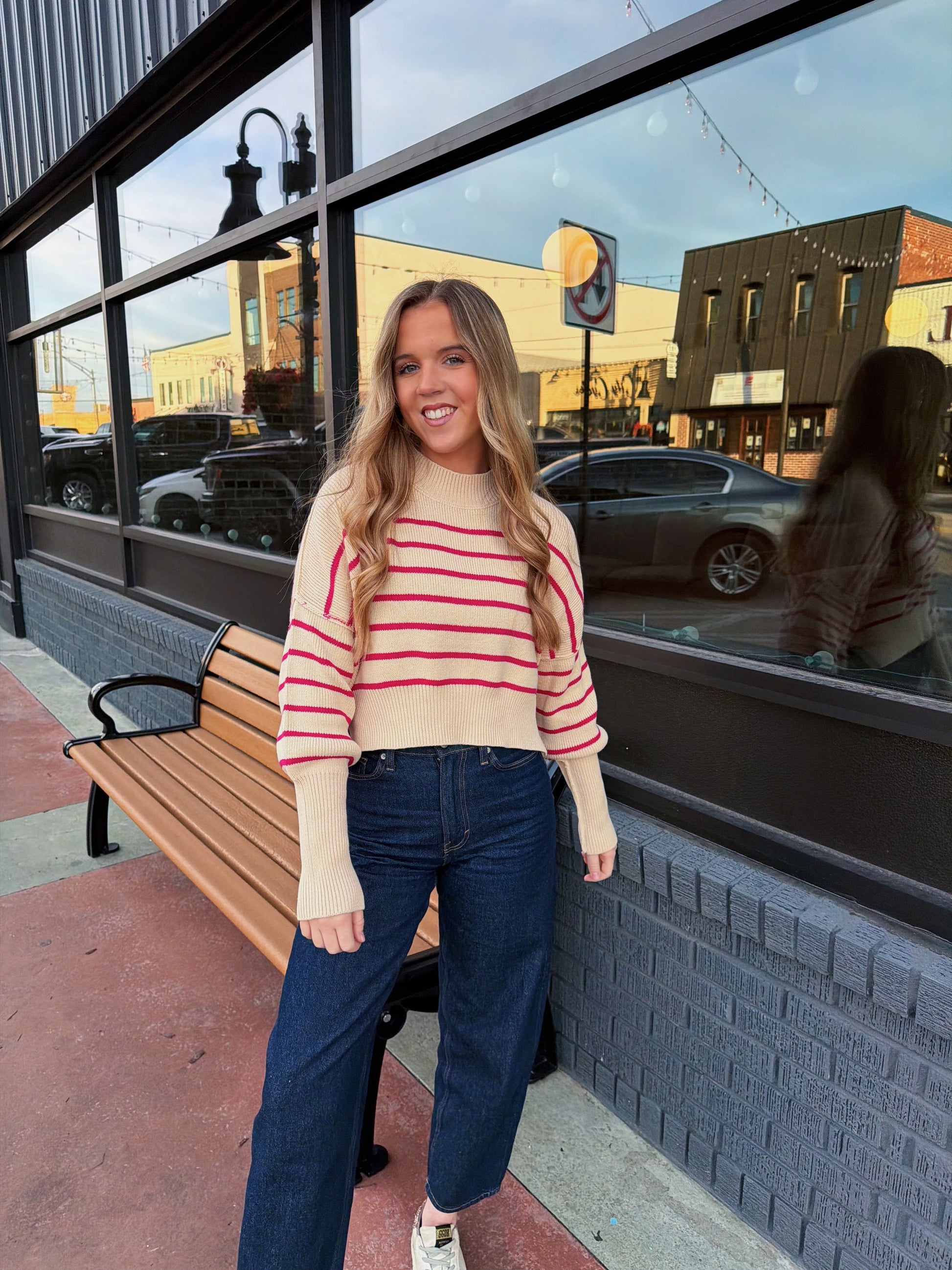 Woman in a striped sweater and jeans standing in front of a store window.