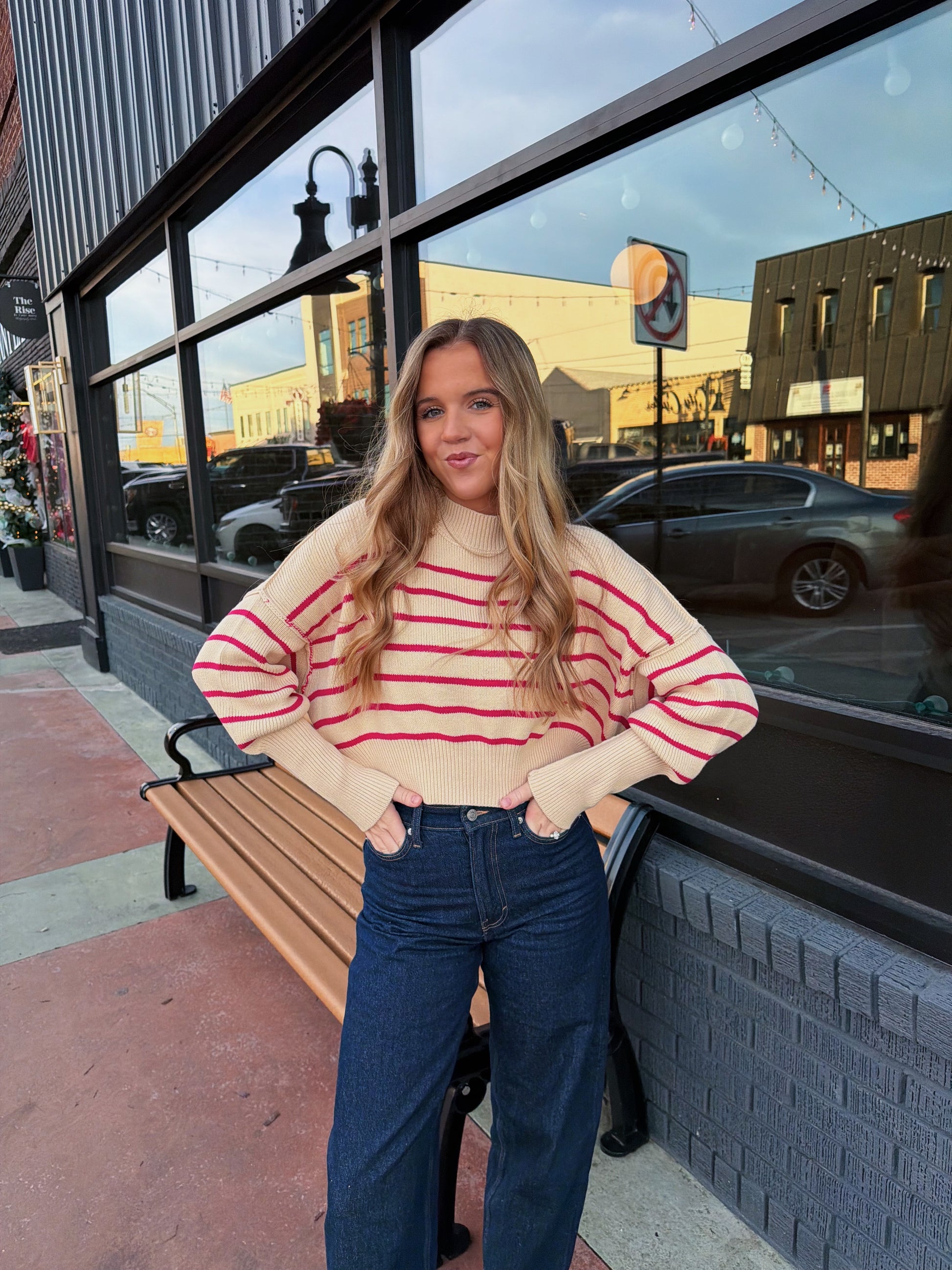 Woman in a striped sweater and jeans standing on a sidewalk with a building in the background