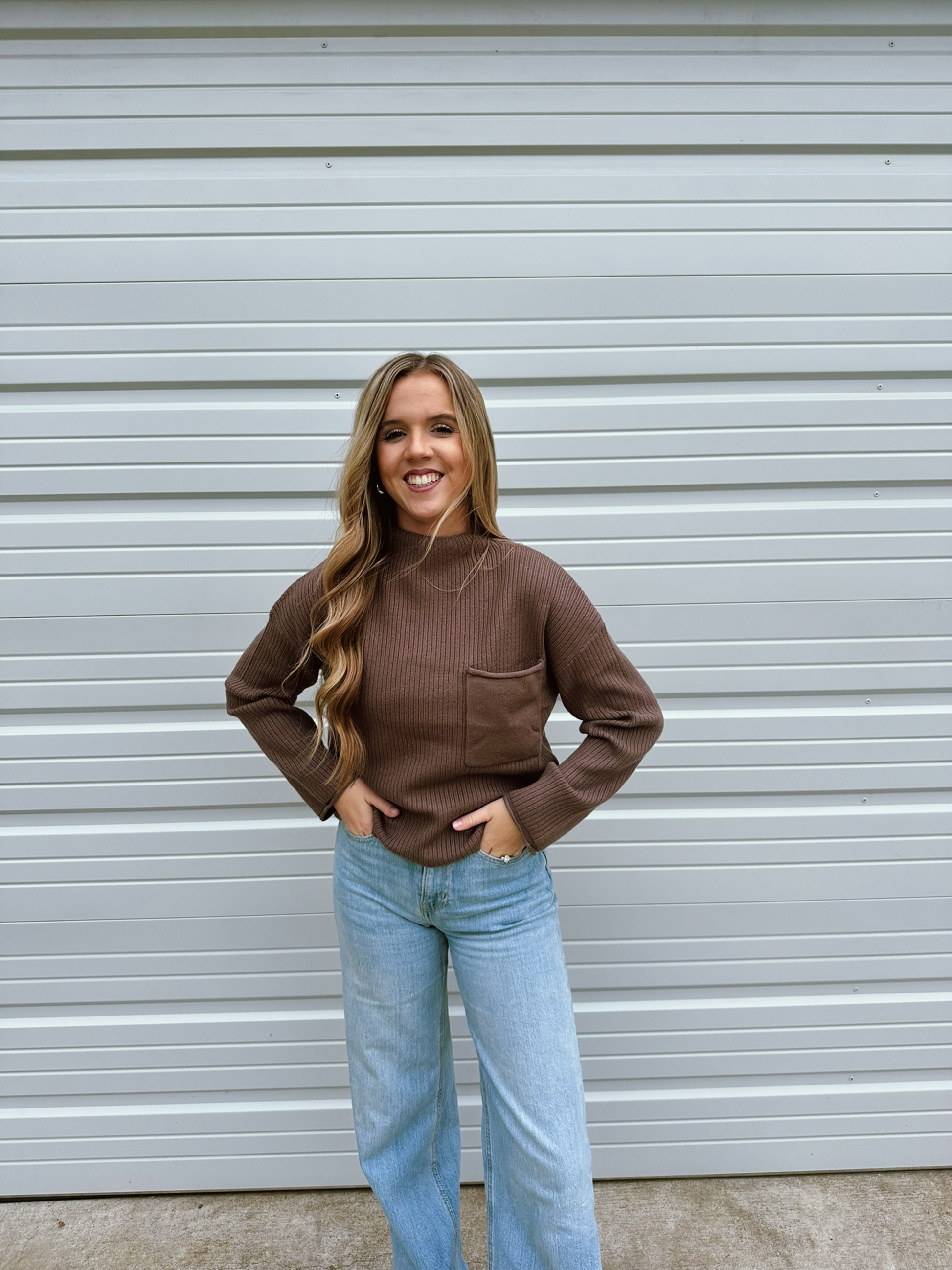 Woman wearing a brown sweater and light blue jeans standing 